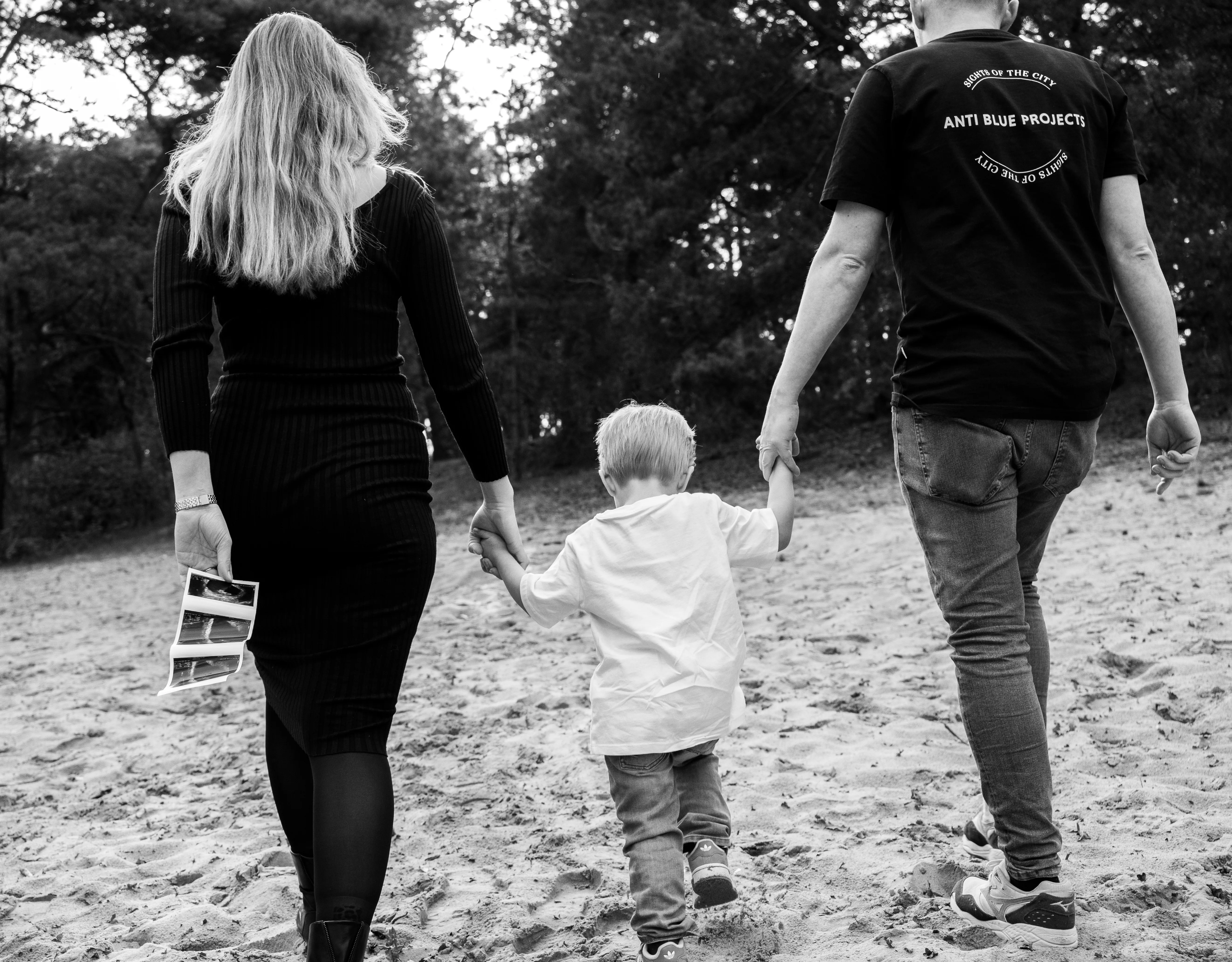 Gezin loopt hand in hand over een zandpad langs het bos, vastgelegd in zwart-wit