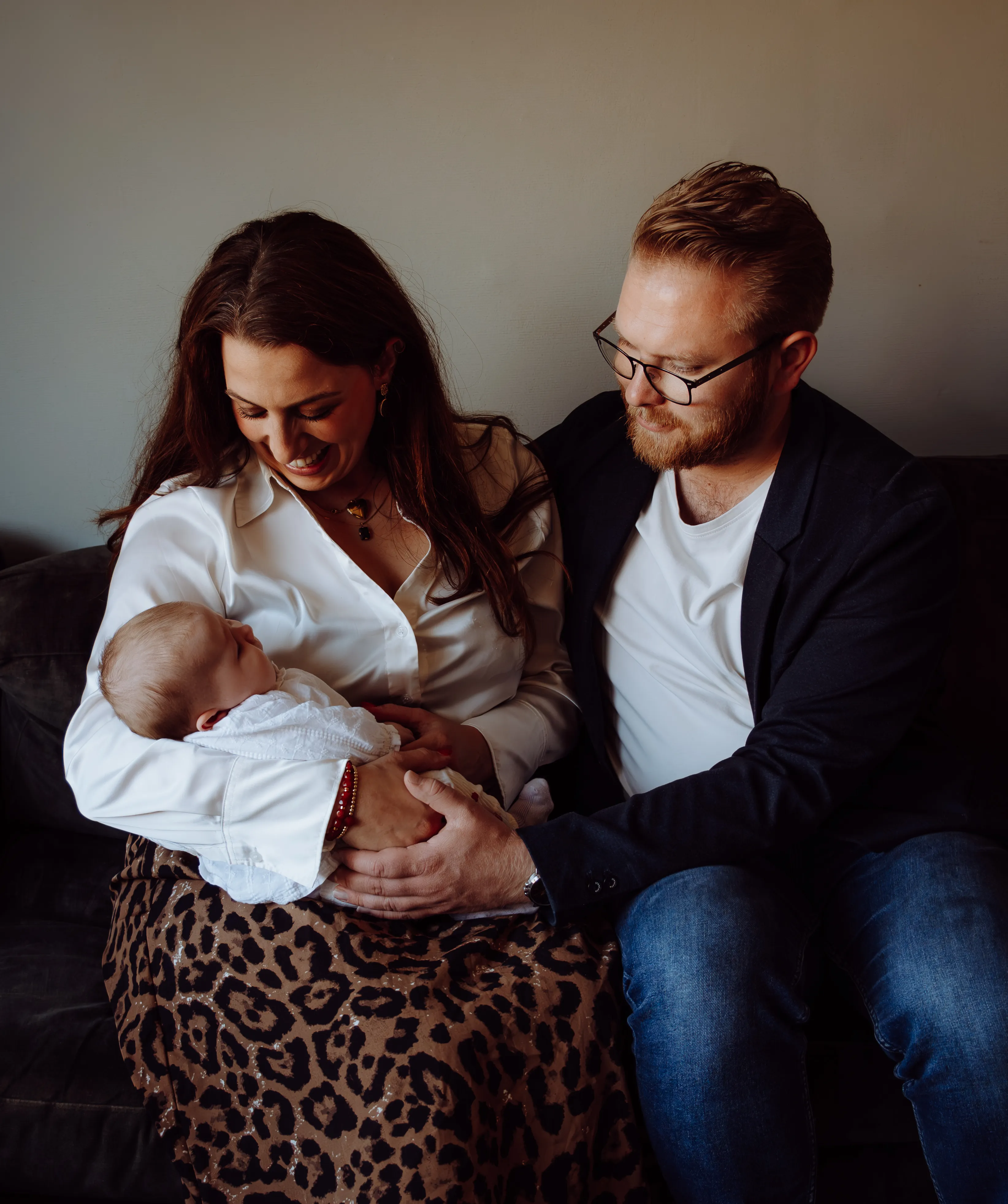 Ouders kijken glimlachend naar hun pasgeboren baby op de bank thuis
