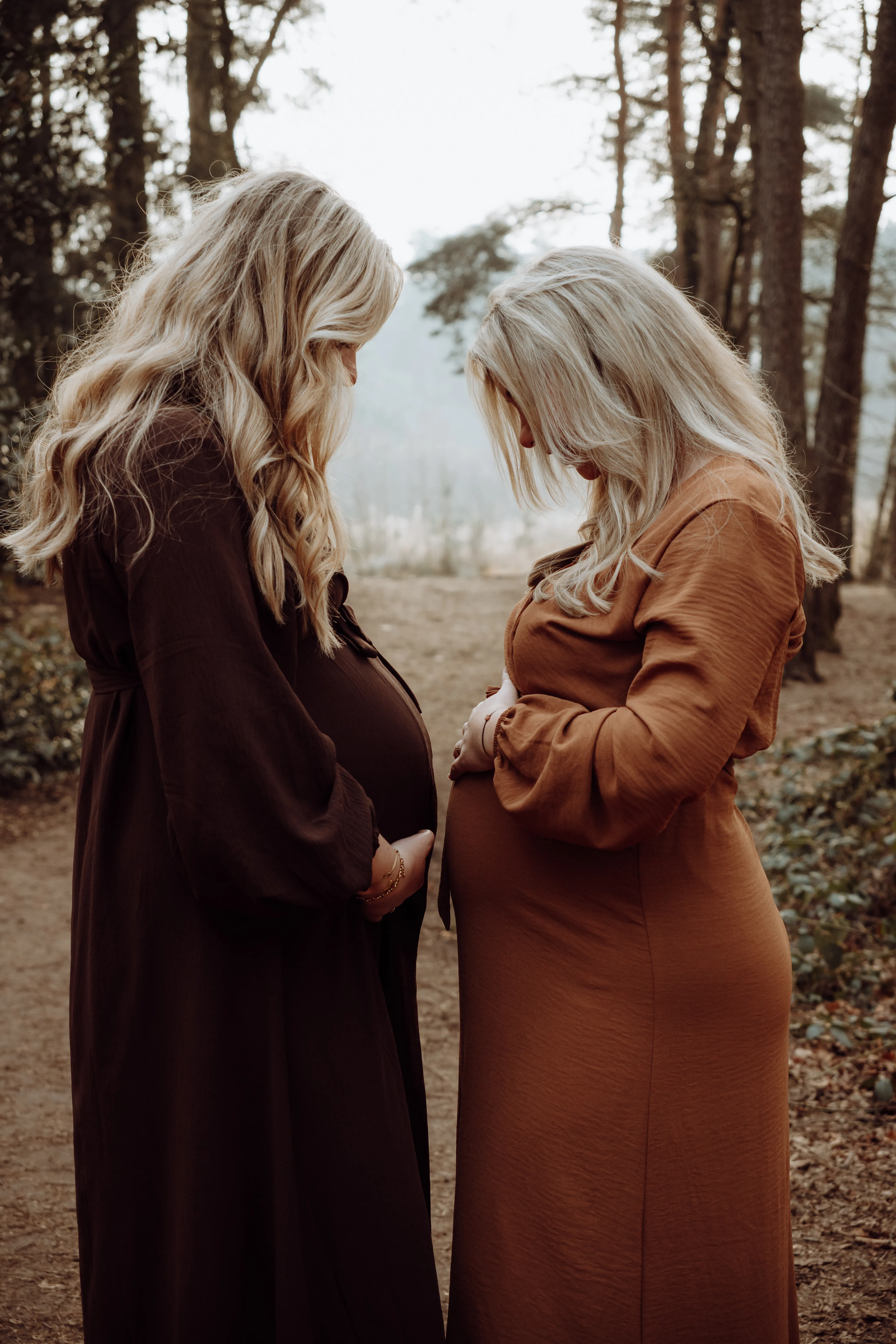 Twee zwangere vrouwen staan tegenover elkaar in het bos, elk met haar handen op de buik