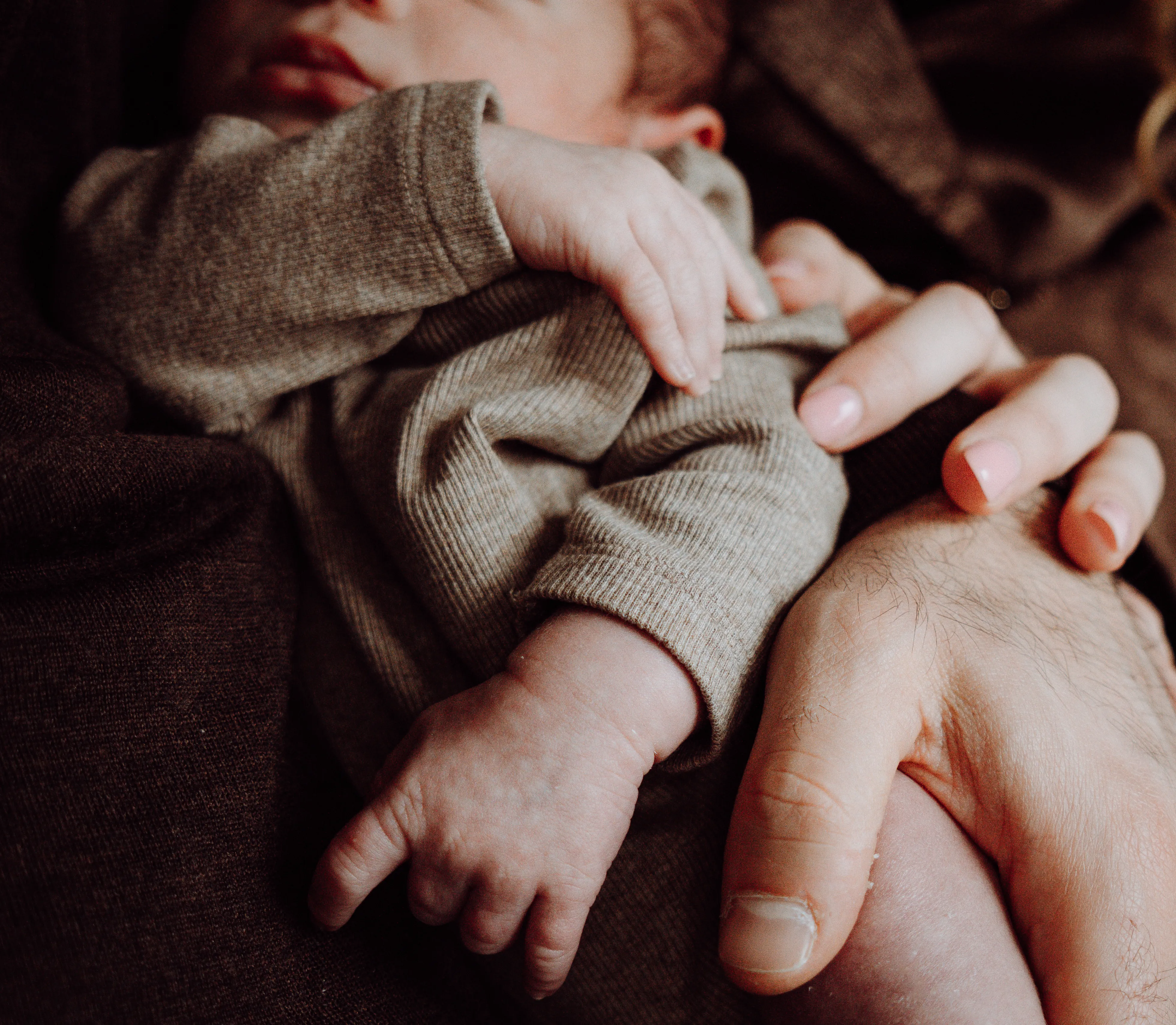 Pasgeboren baby in grijs pakje rustig ondersteund door de handen van een ouder