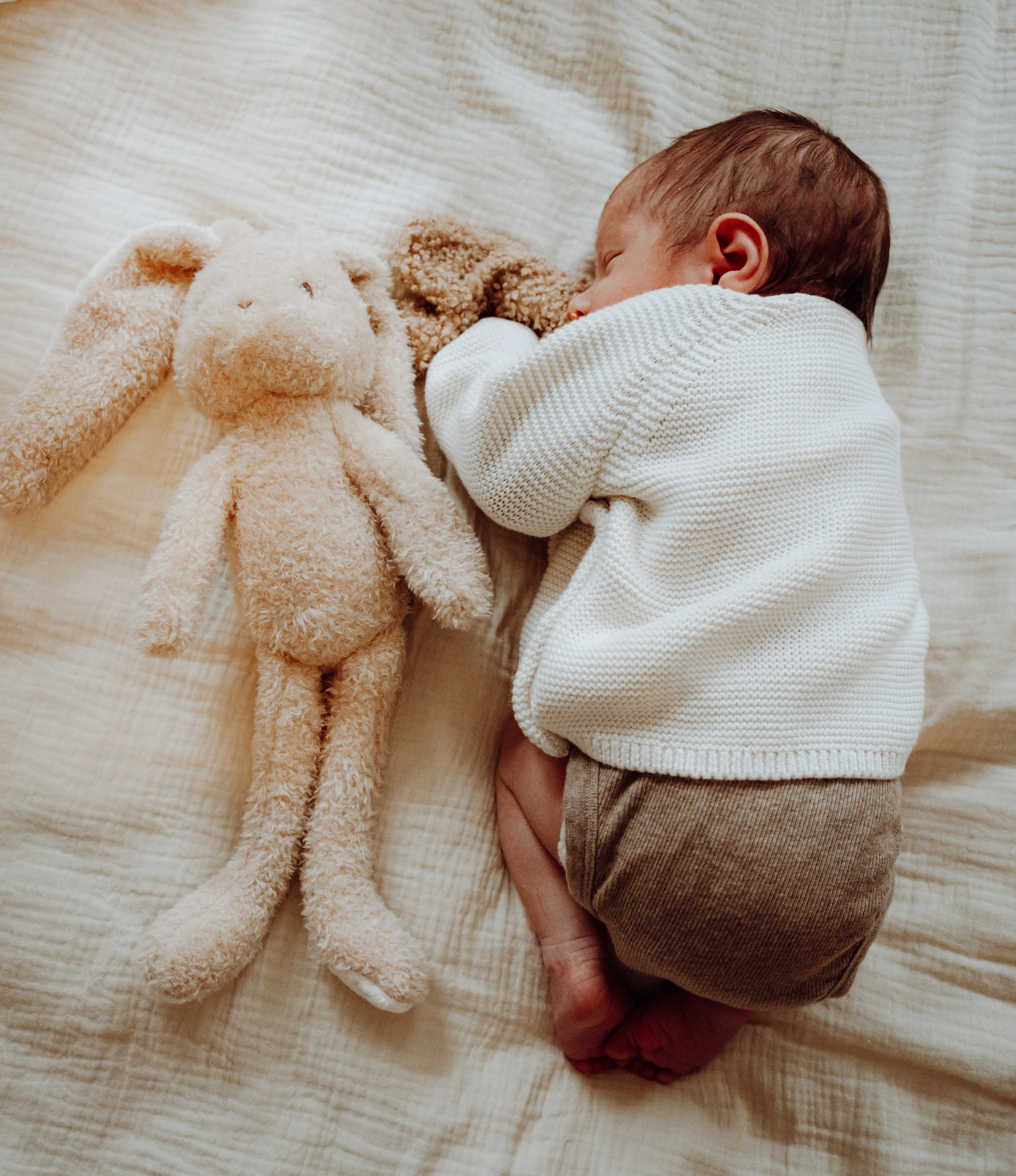 Pasgeboren baby op een zacht dekentje naast een knuffelkonijn en teddybeer