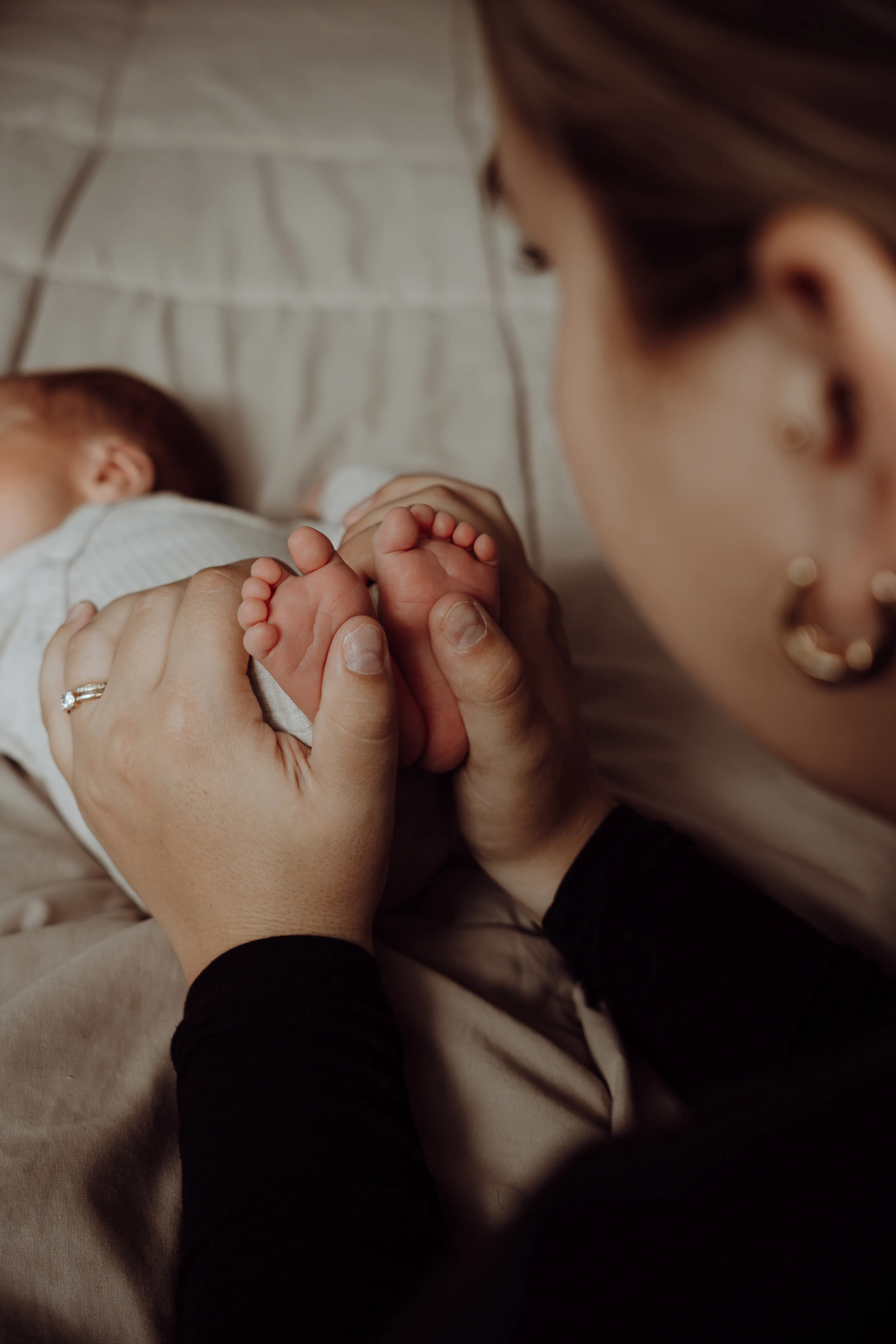 Moeder houdt de blote voetjes van haar pasgeboren baby vast op bed