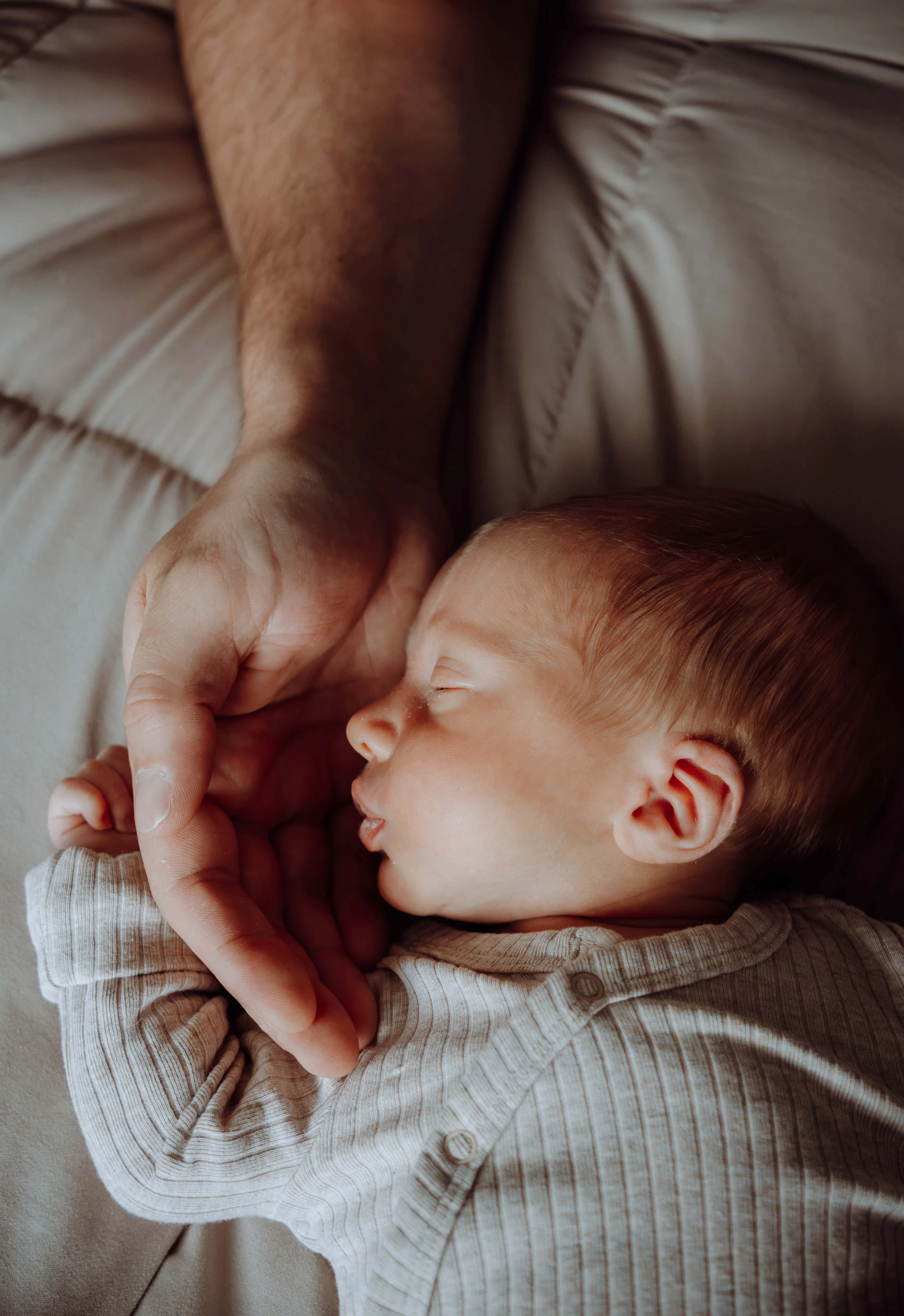 Slapende pasgeboren baby in een zacht pakje met het handje in de hand van een ouder