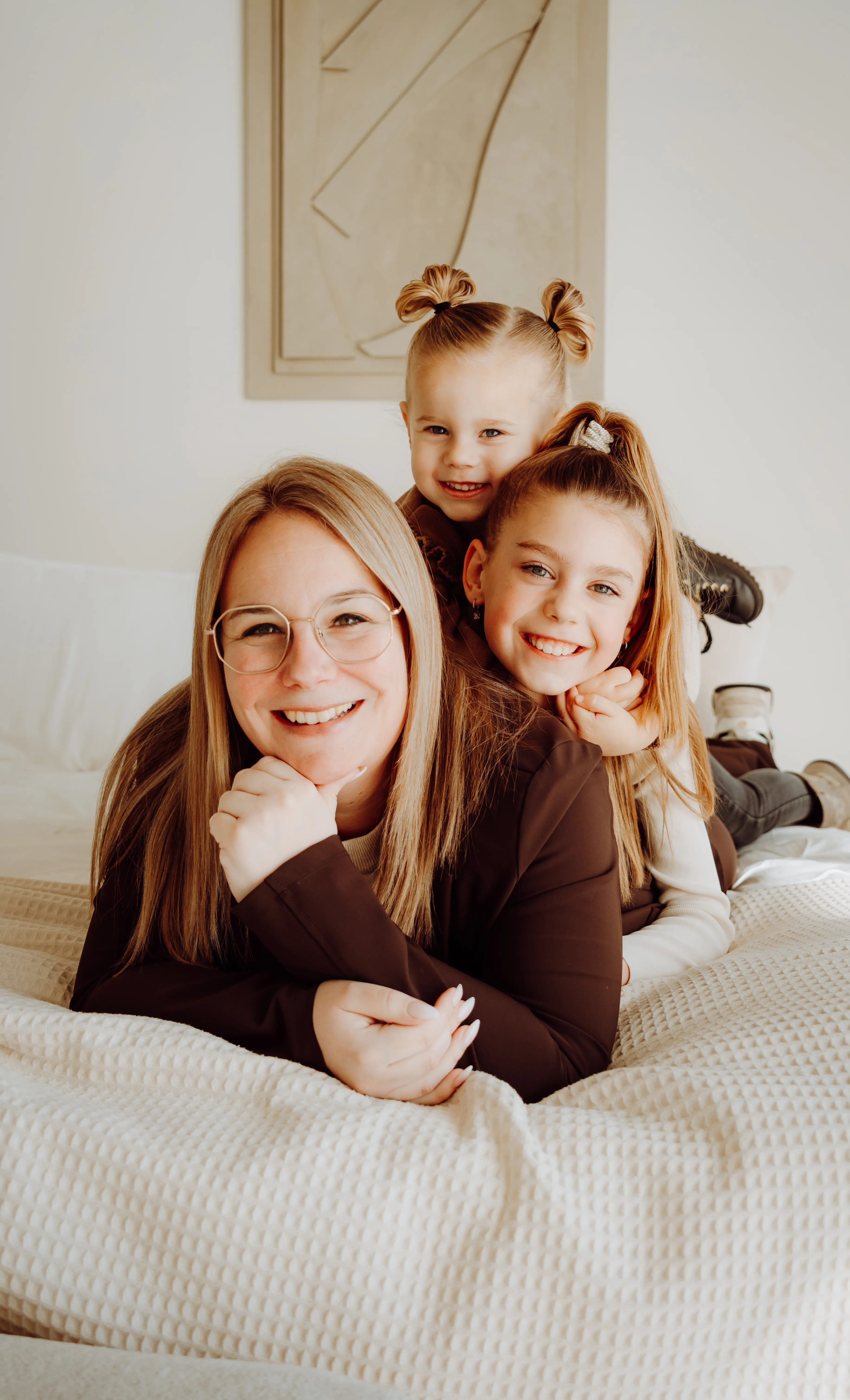 Vrouw ligt samen met twee kinderen lachend op bed tijdens een knusse thuisshoot