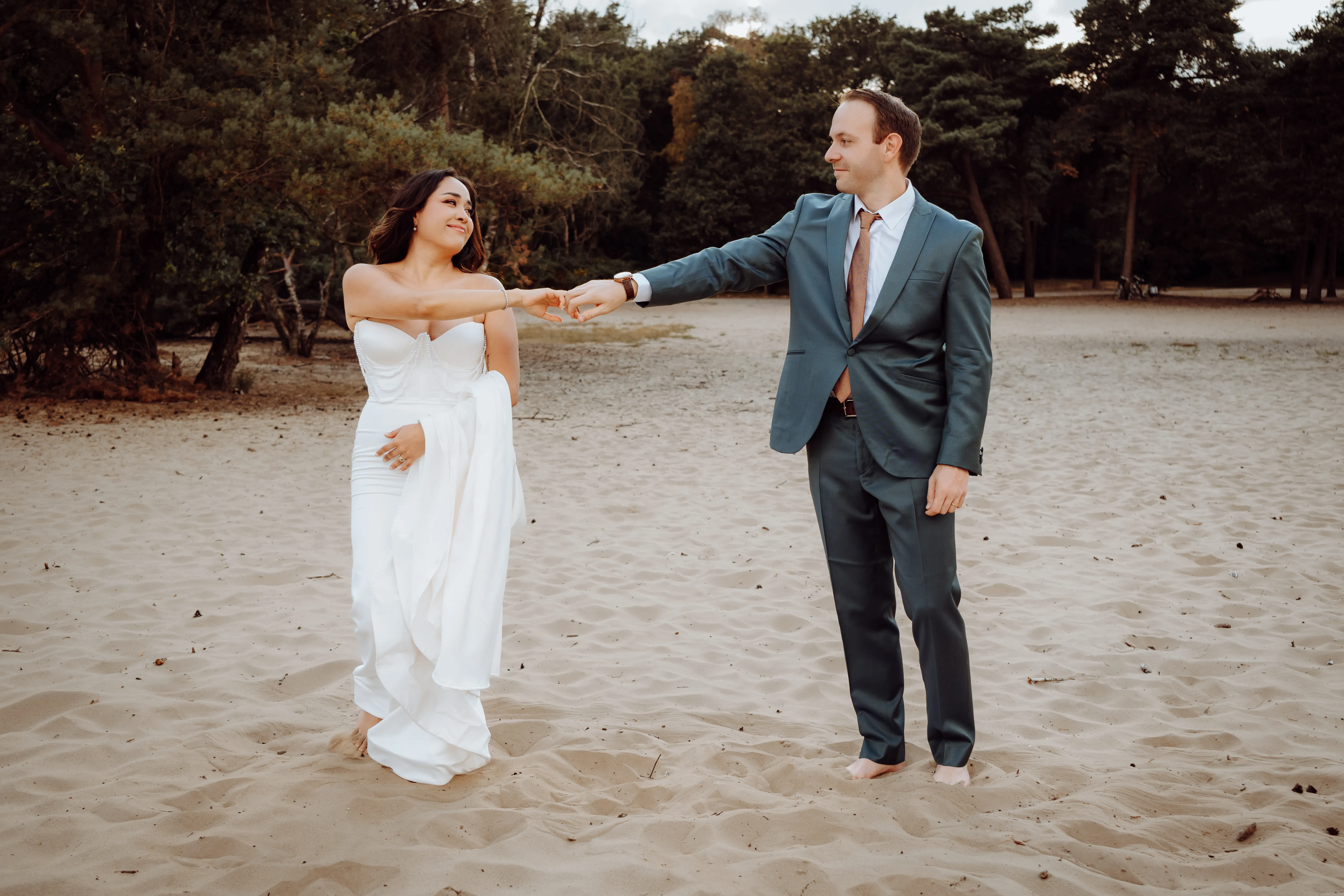 Stel danst hand in hand op het zandstrand met de pijnbomen erachter in warme avondzon