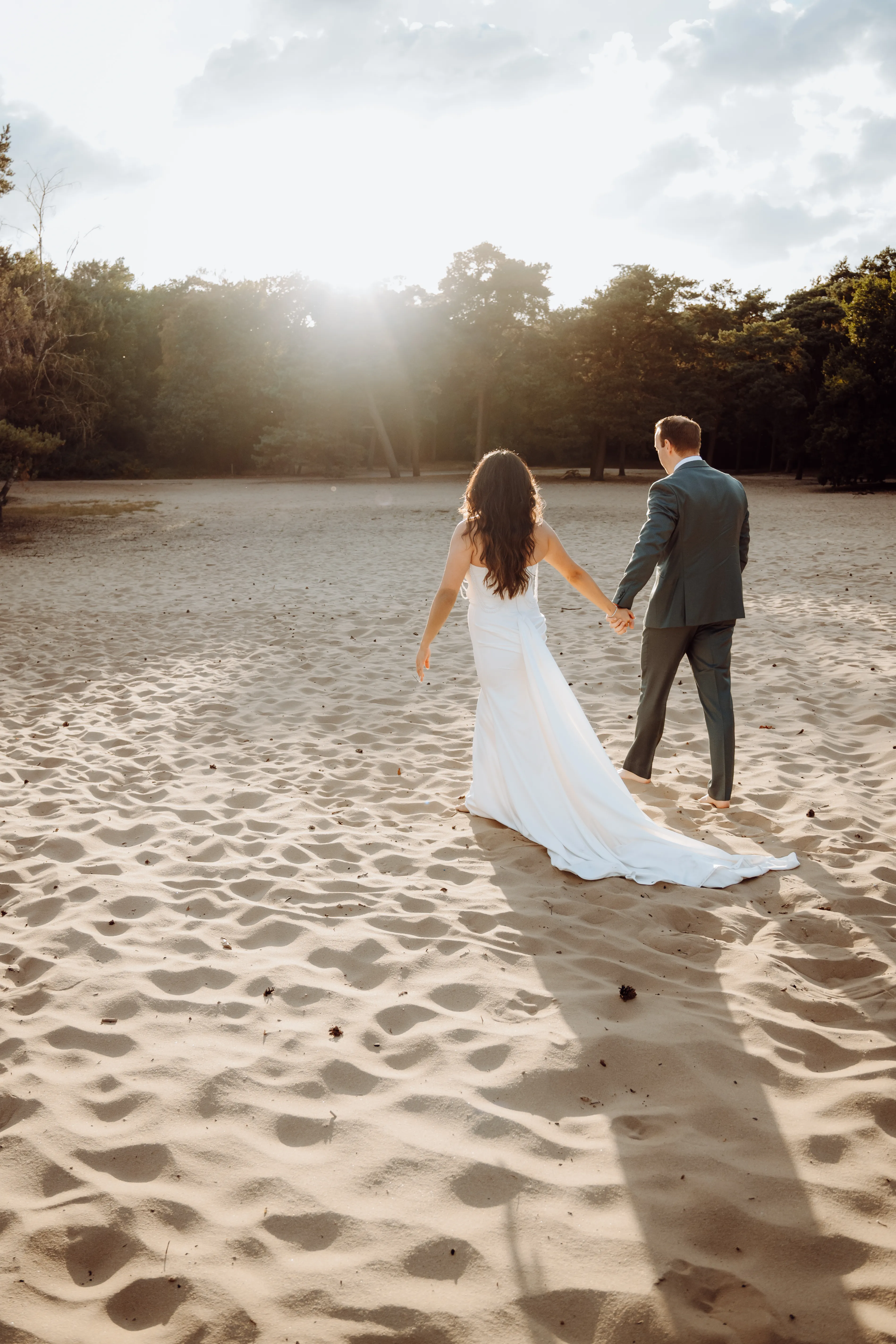 Stel loopt hand in hand richting de ondergaande zon over het zanderige duinlandschap